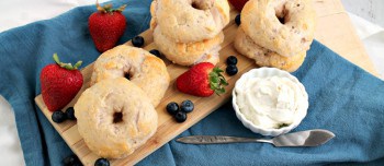Mixed berry Greek yogurt bagels and berries on a wooden tray next to a bowl of cream cheese