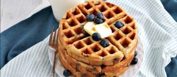 Double blueberry Greek yogurt waffles stacked on a plate and topped with blueberries and butter