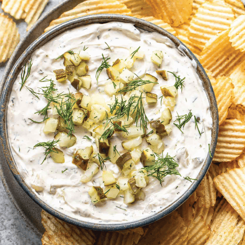 dill pickle dip in a bowl surrounded by wavy potato chips