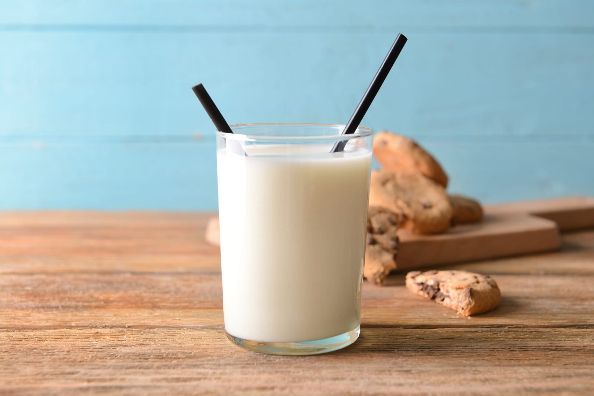 Glass of fresh milk with cookies on wooden table.