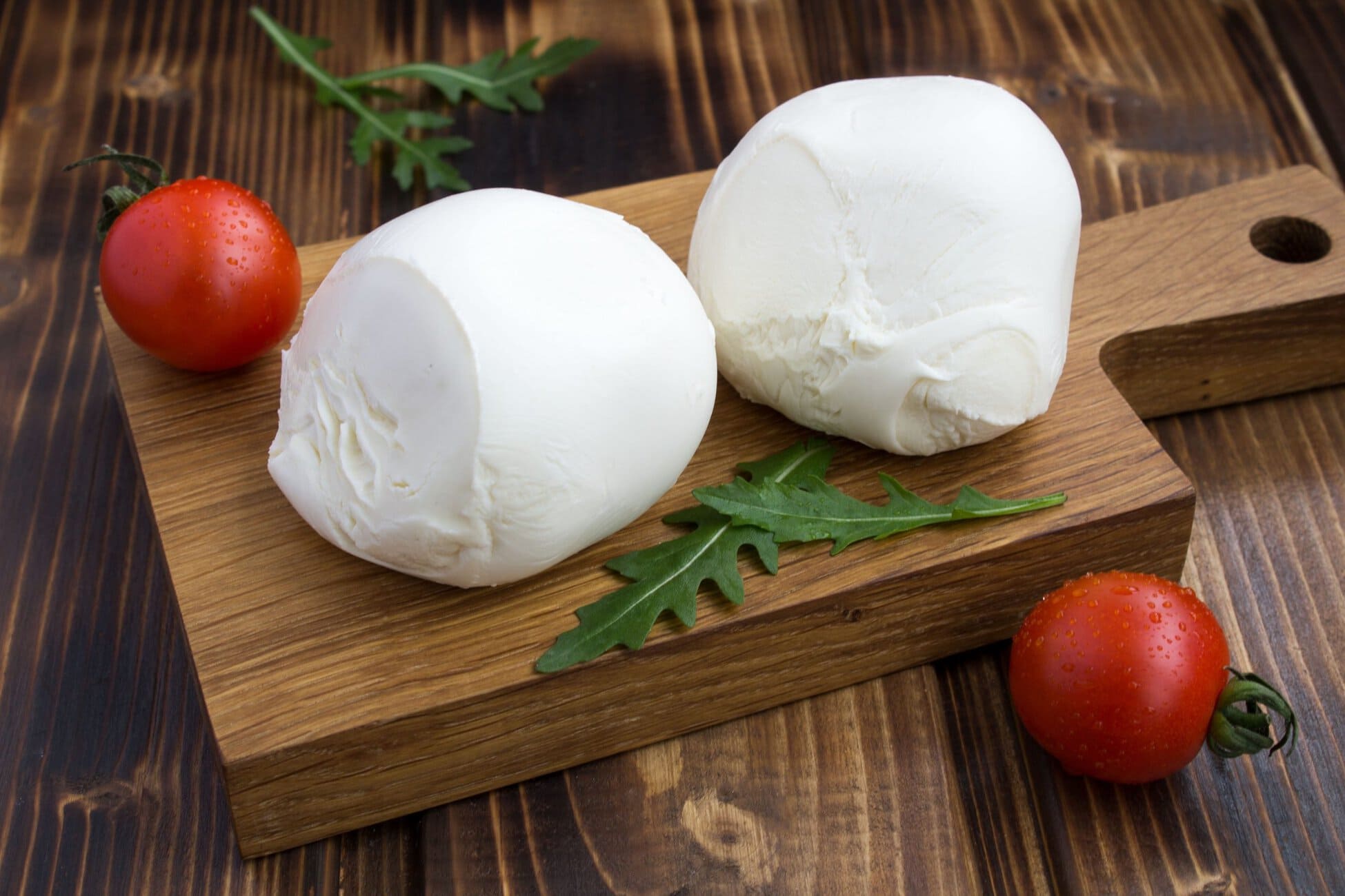 Fresh mozzarella cheese balls with tomatoes and arugula on wooden board.