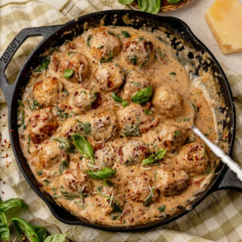 Marry me chicken meatballs in a cast iron skillet on a table with basil, tomatoes and parmesan