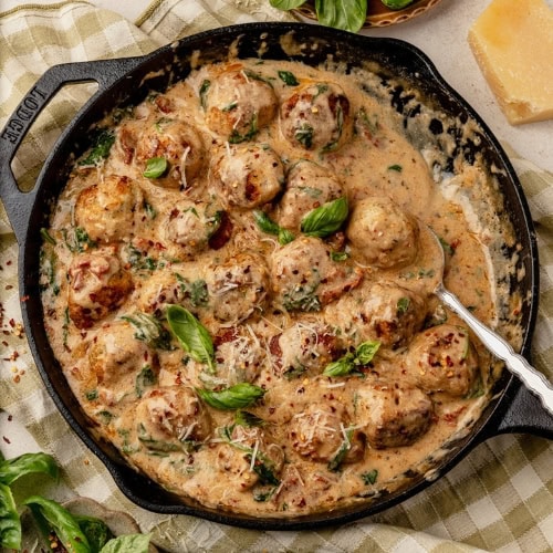 Marry me chicken meatballs in a cast iron skillet on a table with basil, tomatoes and parmesan